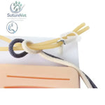 Medical practice pad with a beige and black braided cord and white clip securing yellow rubber tubes for knot-tying training kit