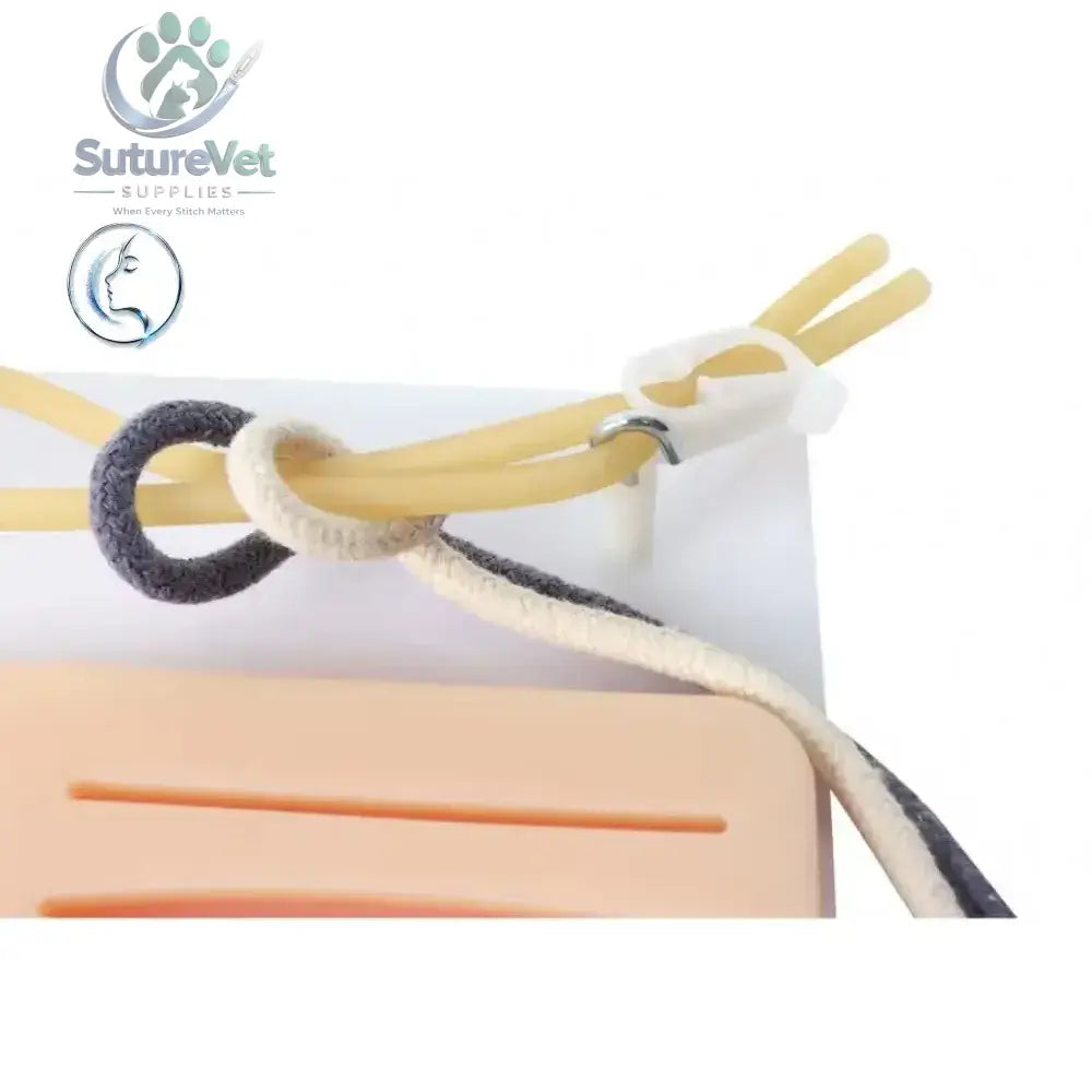 Medical practice pad with a beige and black braided cord and white clip securing yellow rubber tubes for knot-tying training kit
