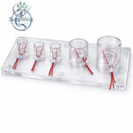 Clear plastic tray with five transparent cylindrical holders containing red wires and white connectors for vascular ligation training